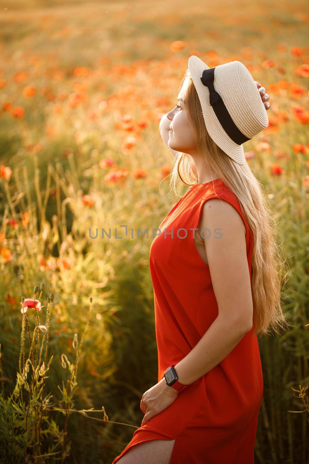 Happy cheerful woman walking on blooming field poppies. Red flowers. A blonde in a red short dress and a hat.