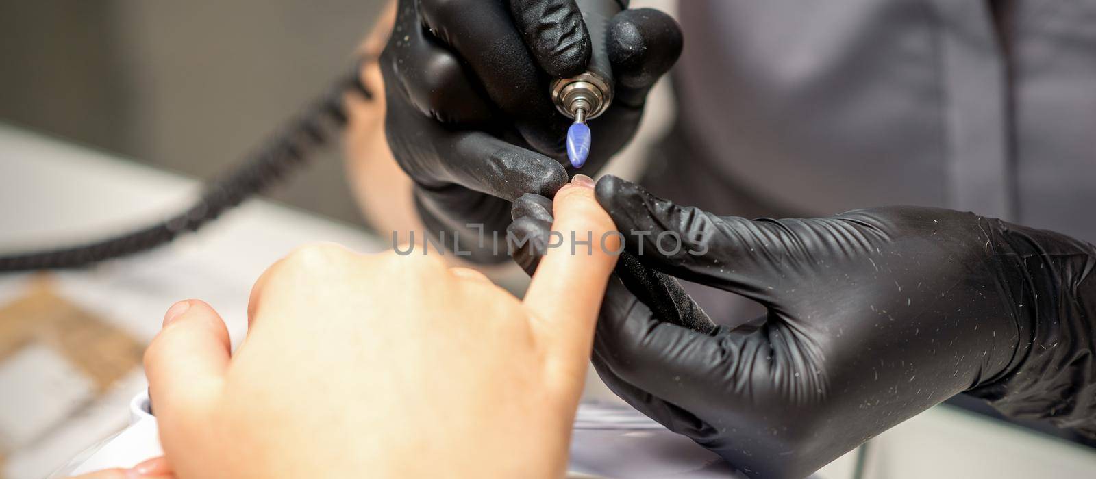Manicure master uses electric nail file machine in a nail salon, close up. by okskukuruza