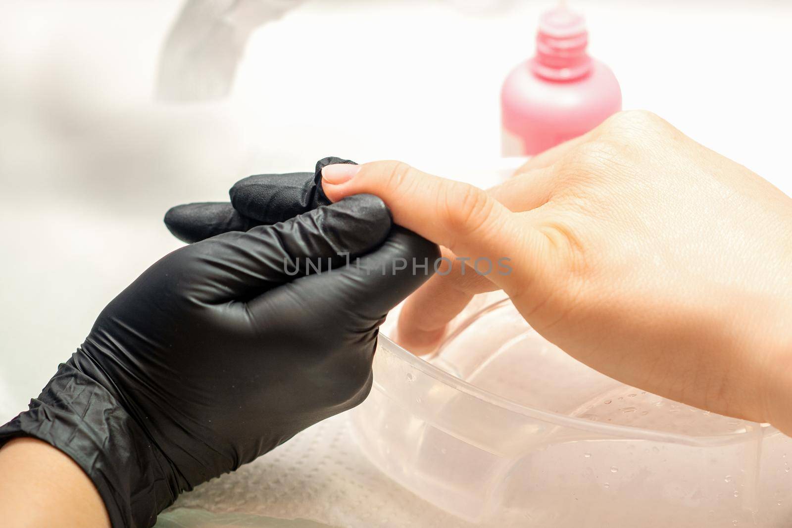 Close up professional manicure master holds the female hand of the customer and disinfects nails in a nail salon