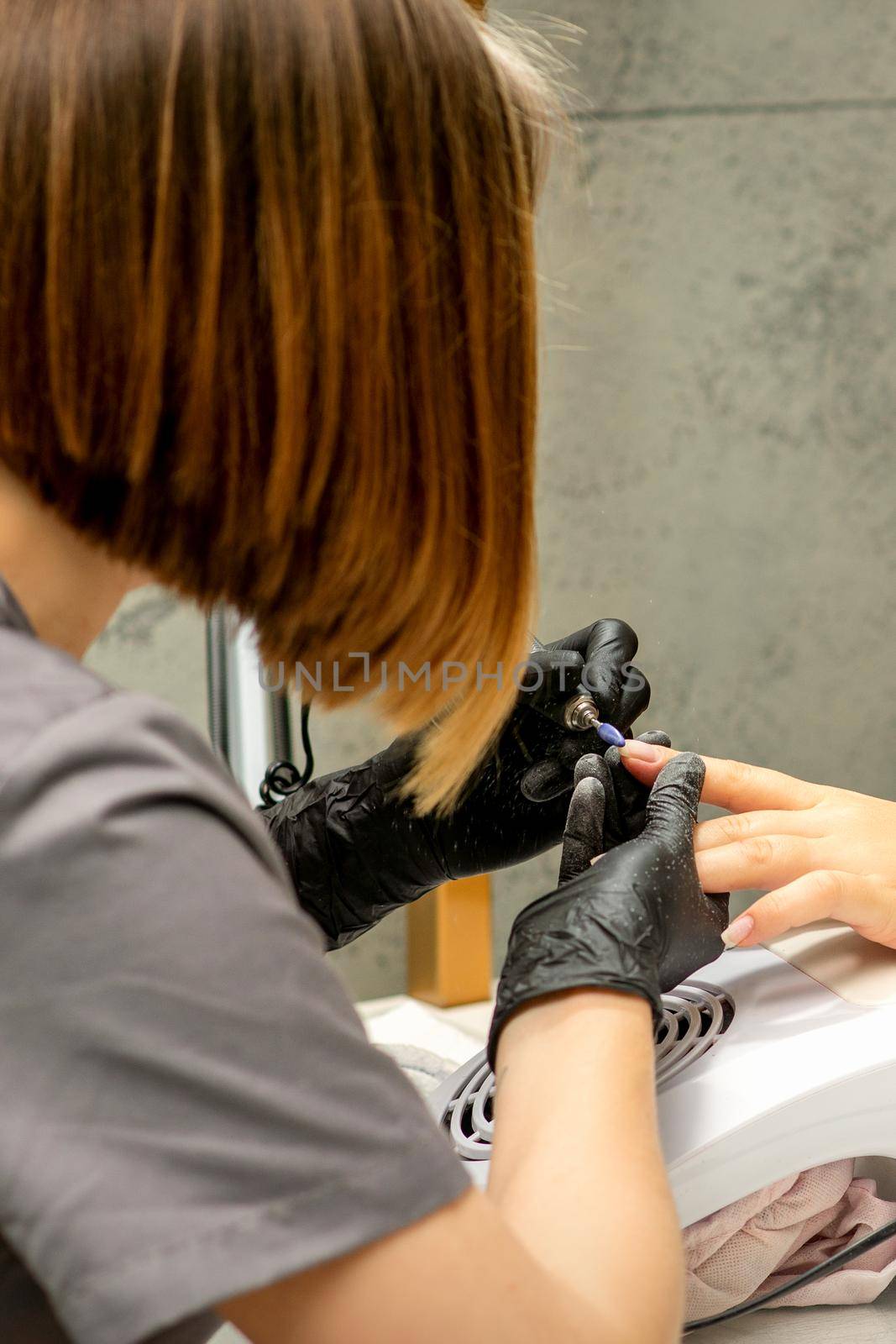 Manicure master in rubber gloves applies an electric nail file to remove the nail polish in a nail salon. by okskukuruza