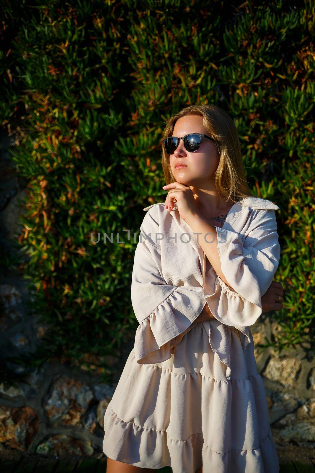 Young beautiful woman in sunglasses walks under the bright sun, she is in a beige short skirt and top
