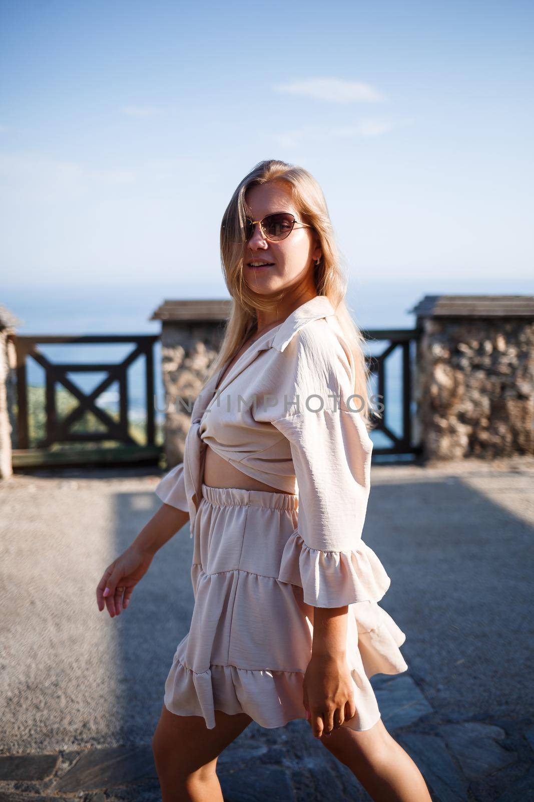 Young woman with long blond hair in a light top and skirt walks on a summer sunny day