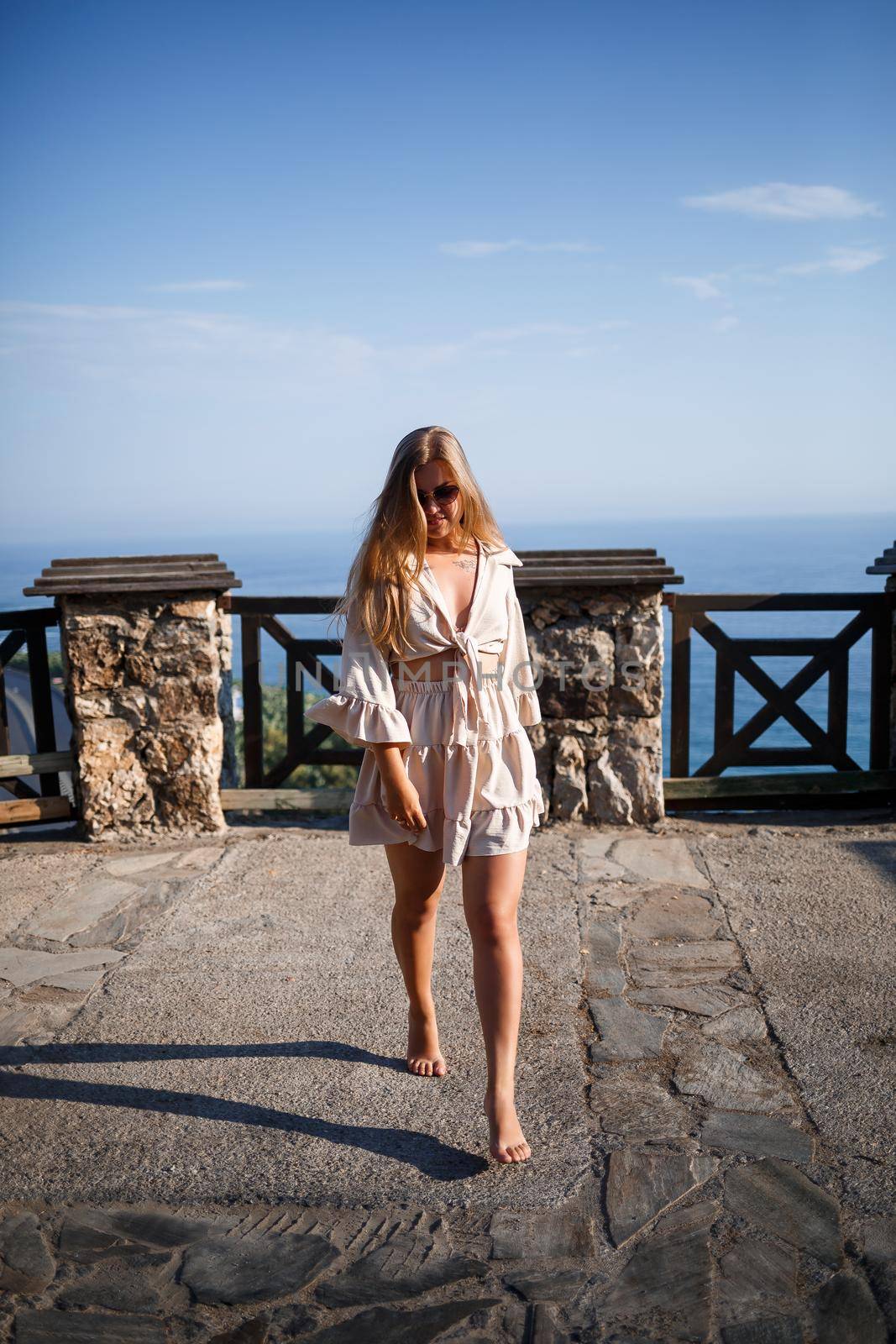 A young woman with long blond hair in a top and a skirt is walking on a summer sunny day. Happy girl with a smile on her face and in sunglasses is walking on a sunny day
