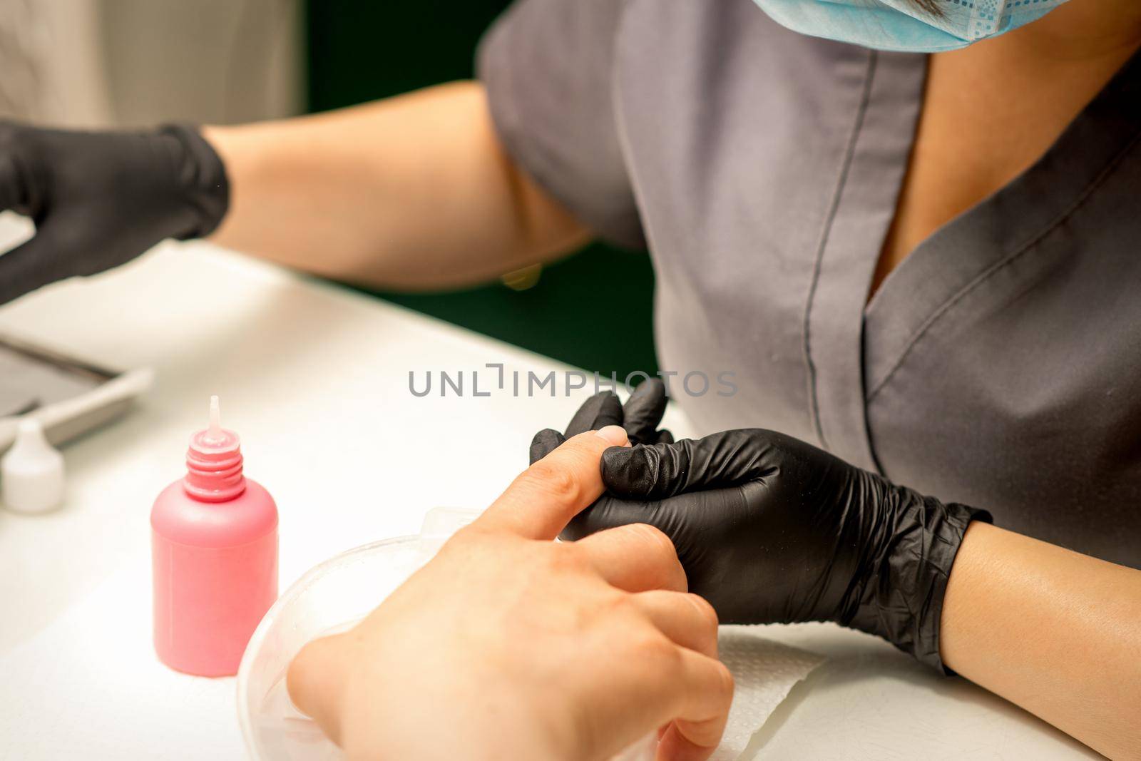 Close up professional manicure master holds the female hand of the customer and disinfects nails in a nail salon. by okskukuruza