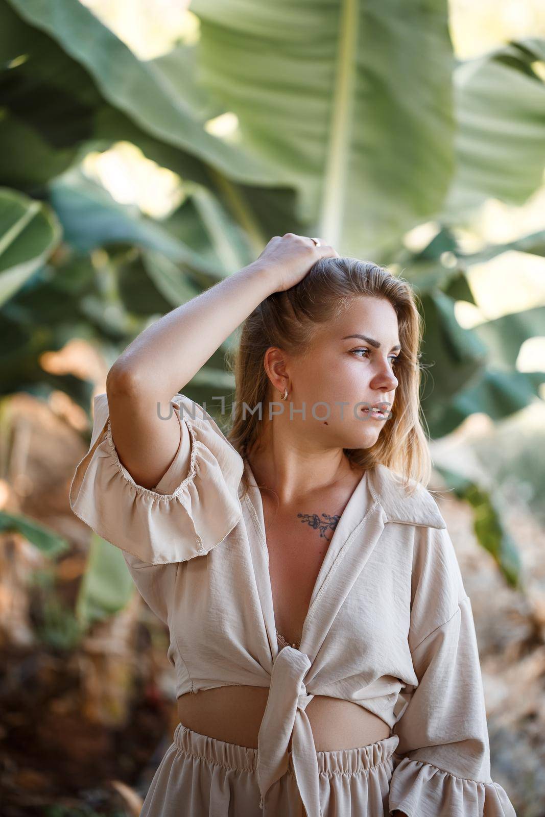 A woman stands near green banana leaves on the island. Tropical trees