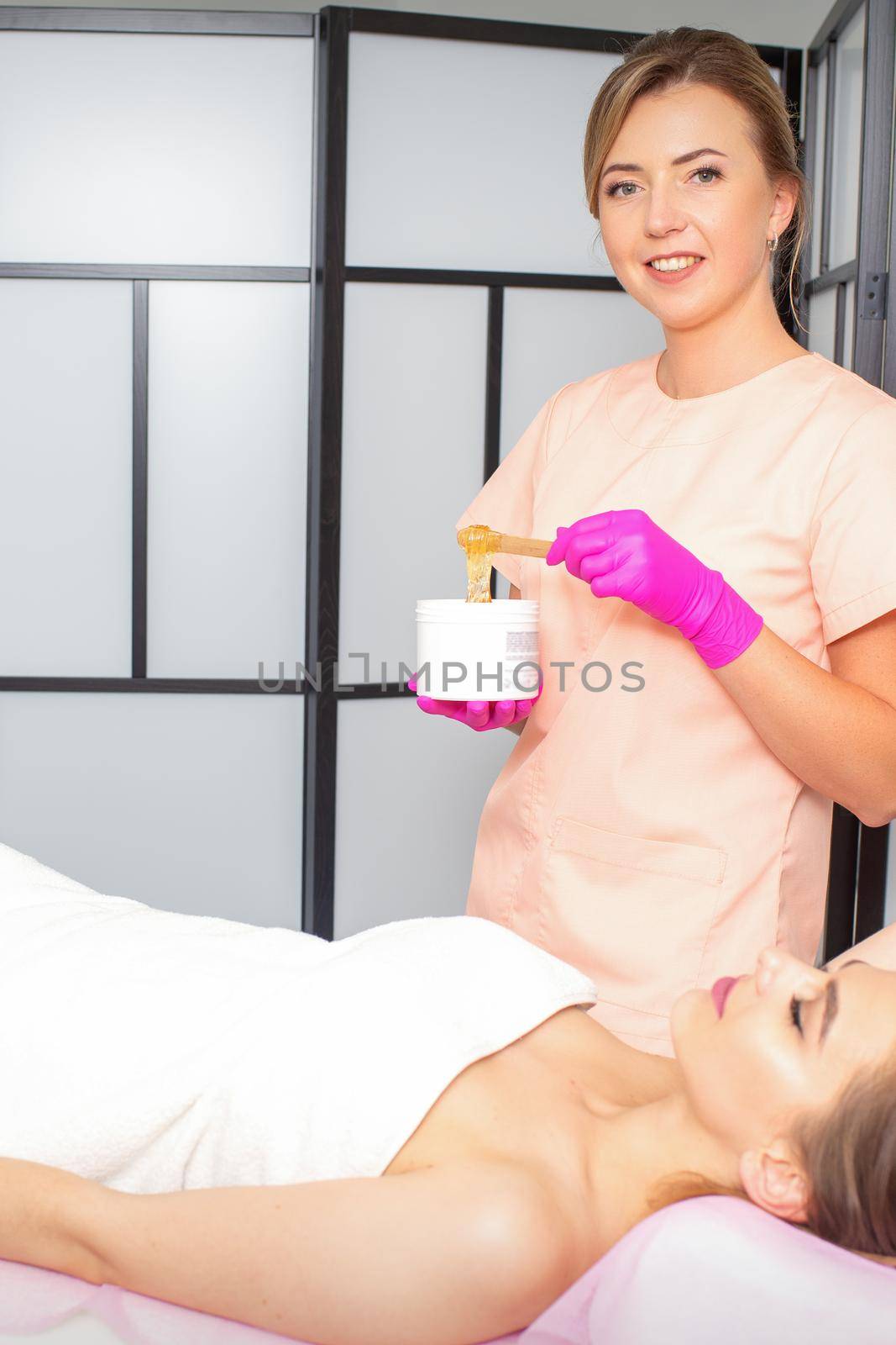 Sugaring. The beautician takes the sugar paste from the jar with a spatula. Lying woman customer waiting for sugaring procedure in the beauty salon