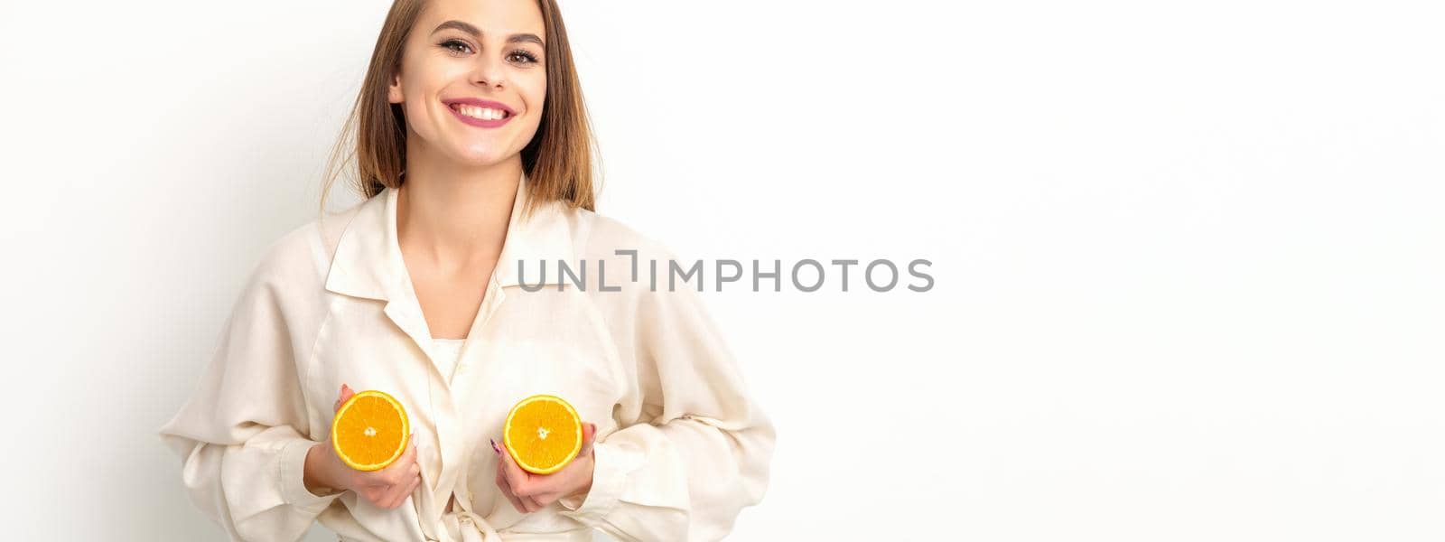 Young Caucasian smiling woman holding slices orange over isolated white background, breast health concept