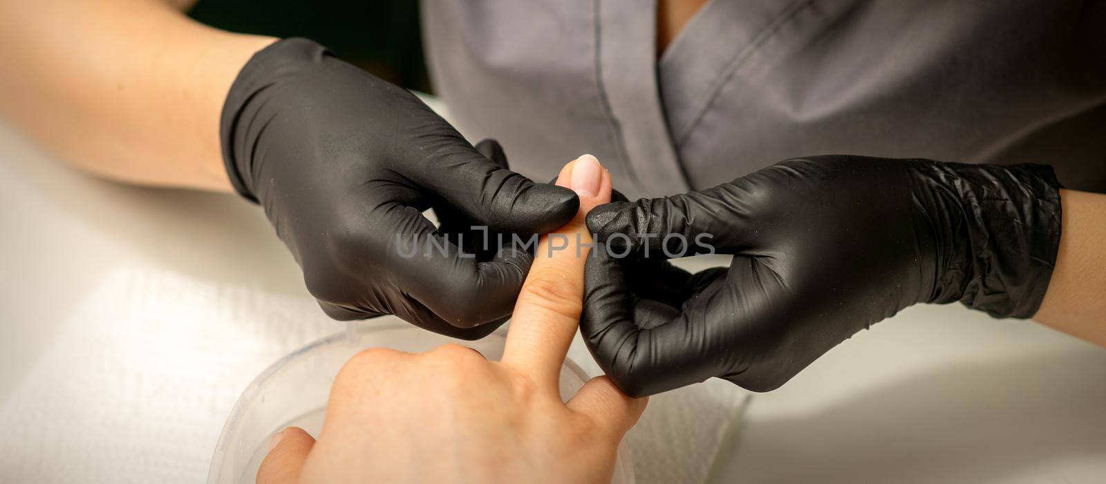 Close up professional manicure master holds the female hand of the customer and checks the manicure in a nail salon. by okskukuruza
