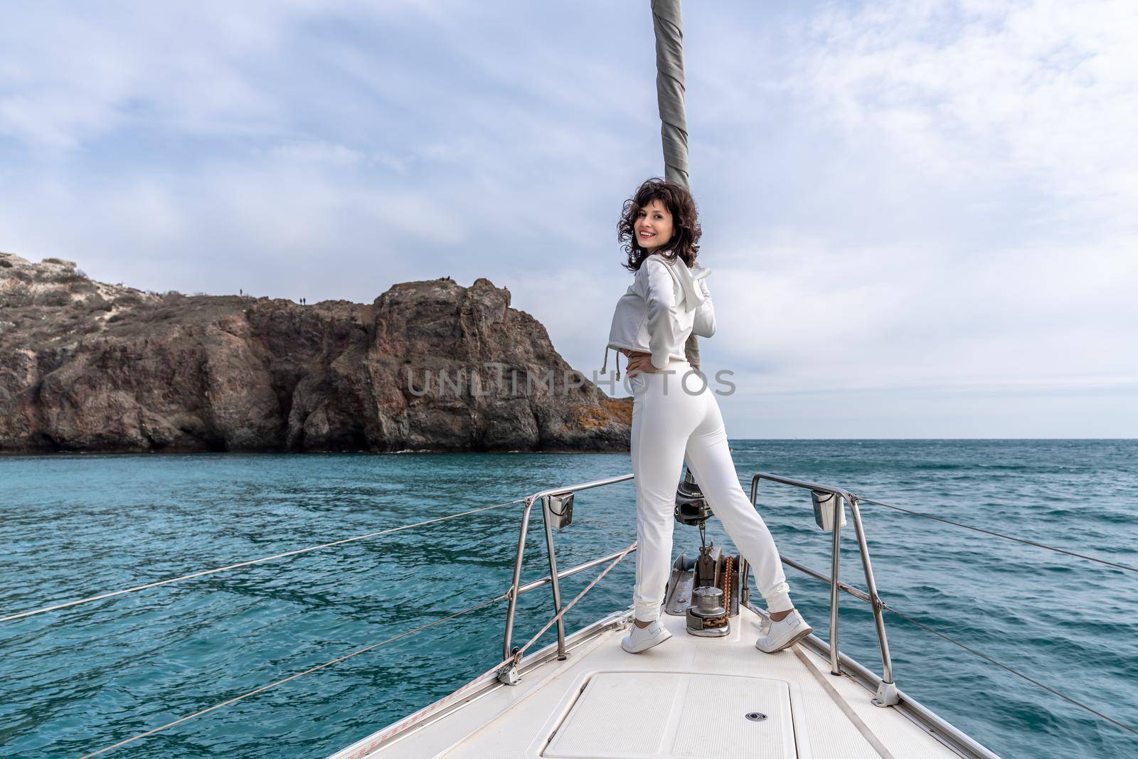 Woman standing on the nose of the yacht at a sunny summer day, breeze developing hair, beautiful sea on background.