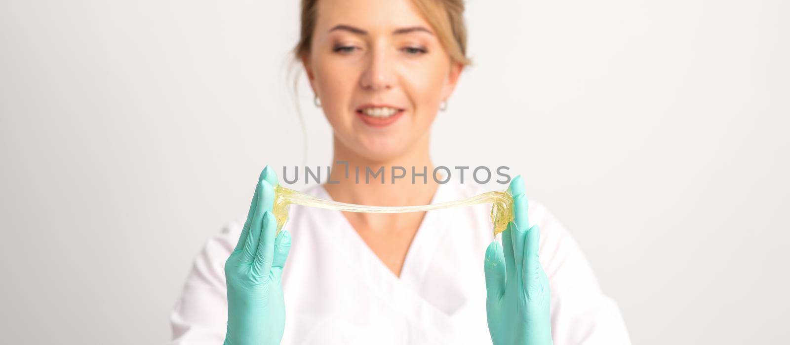 Young caucasian smiling female beautician holding wax for depilation over white background. Yellow sugar paste in hands master of depilation. Epilation concept