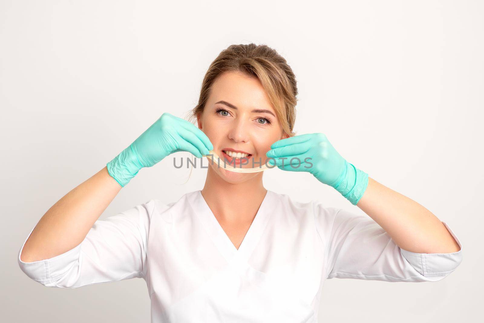 Young caucasian smiling female beautician holding wax for depilation over white background. Yellow sugar paste in hands master of depilation. Epilation concept