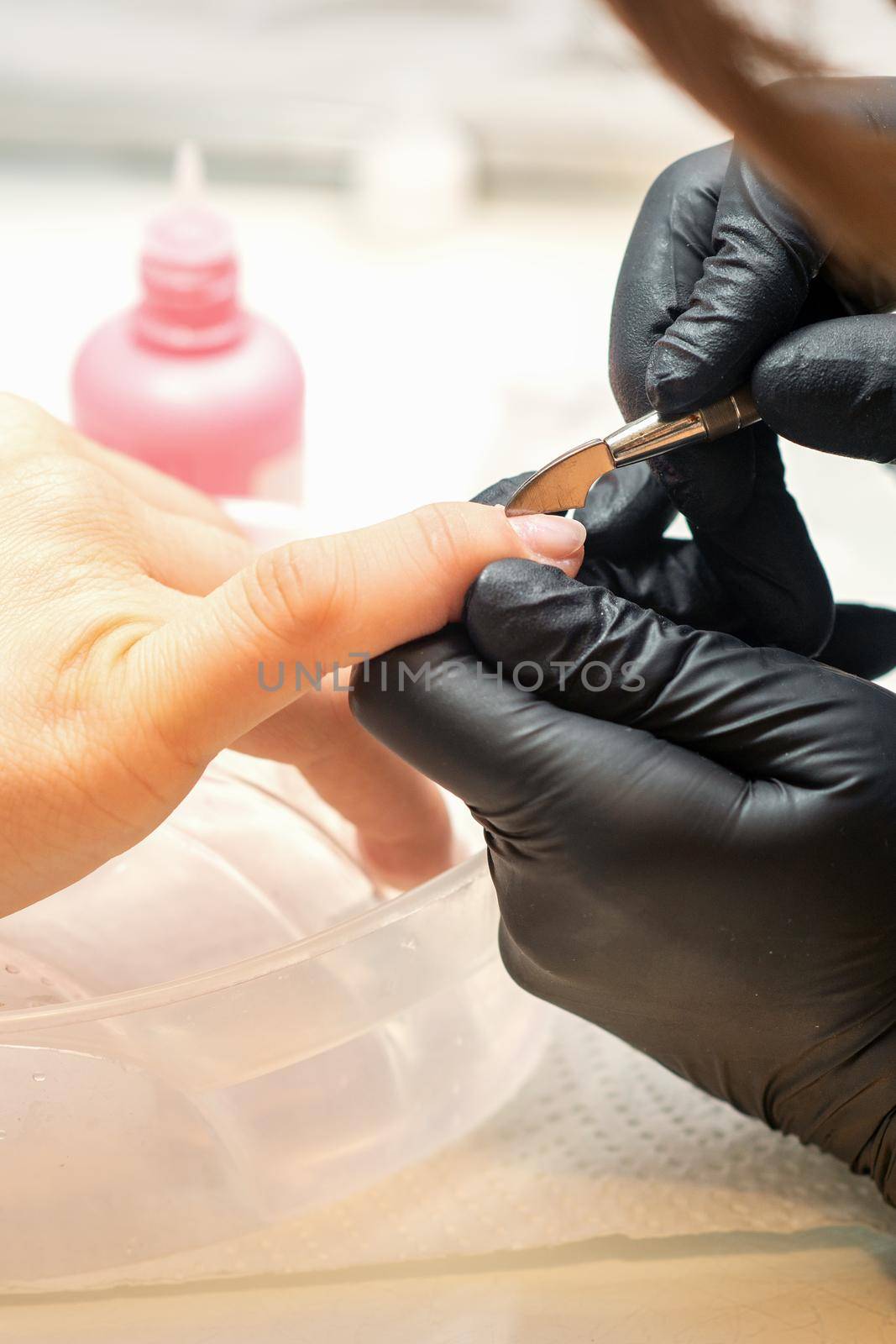 Close up professional manicurist master holding customer hand while using a cuticle pusher in a nail salon. by okskukuruza