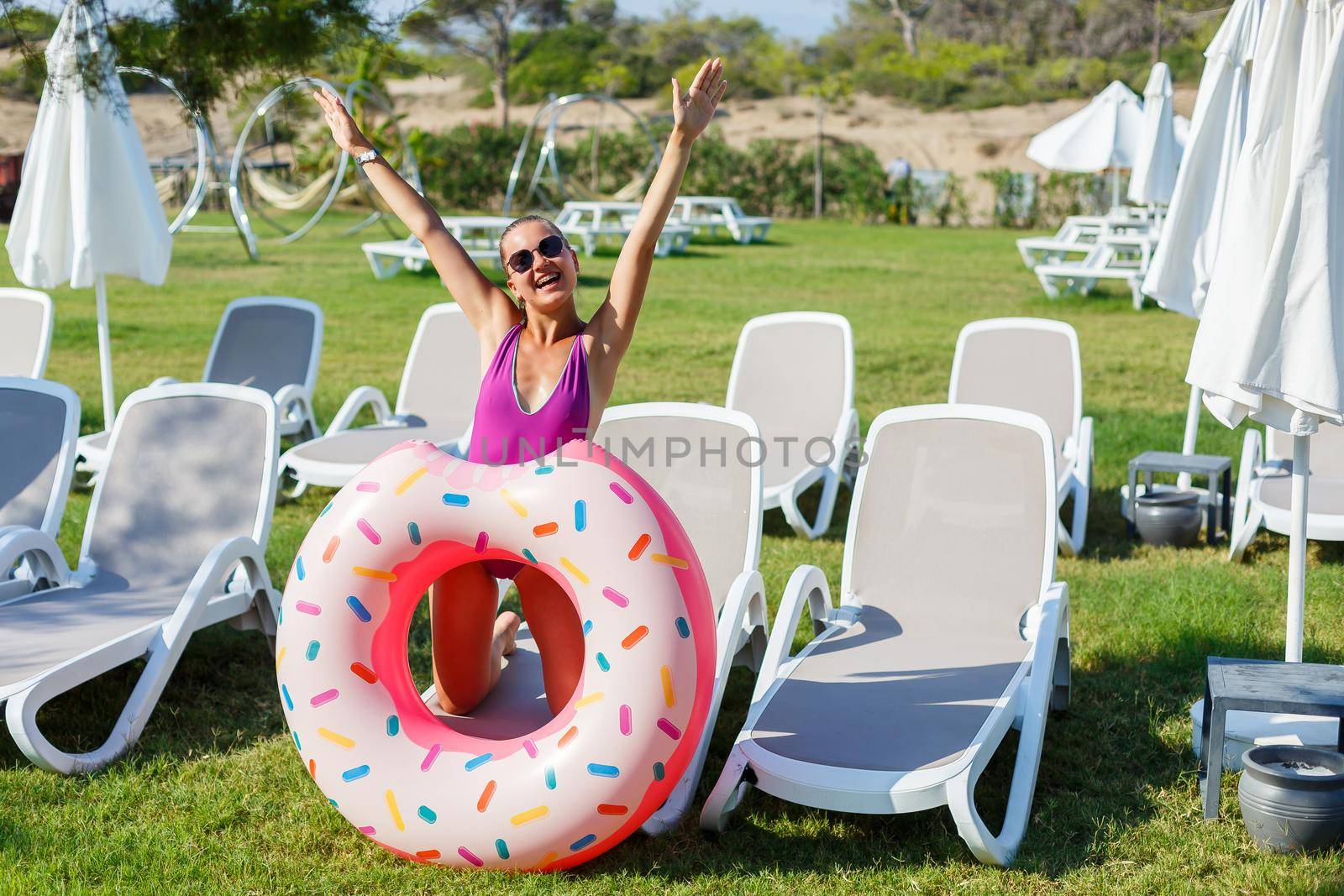 A young woman in a stylish swimsuit and sunglasses holds an inflatable donut ring in her hand. Beautiful happy girl posing and having fun in the sun. Vacation. travel