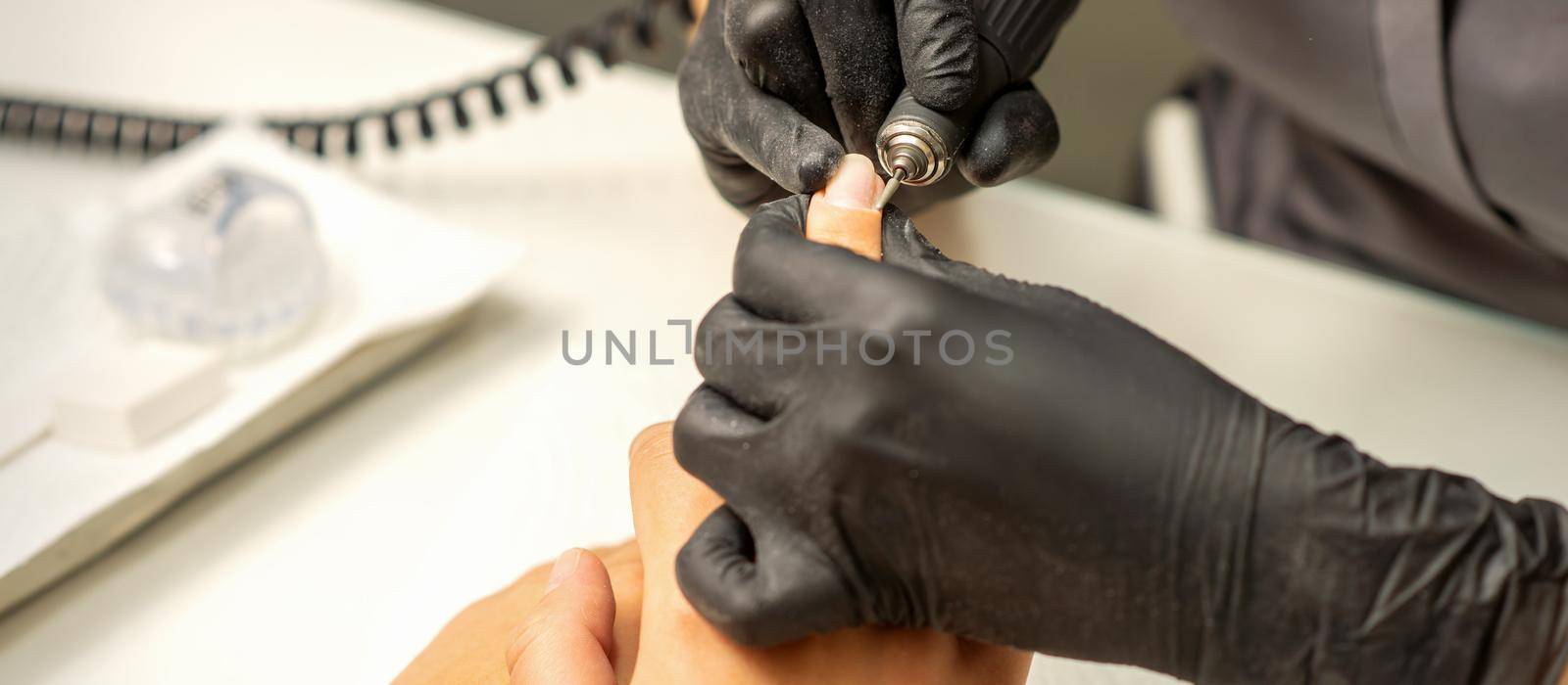 Manicure master uses electric nail file machine in a nail salon, close up