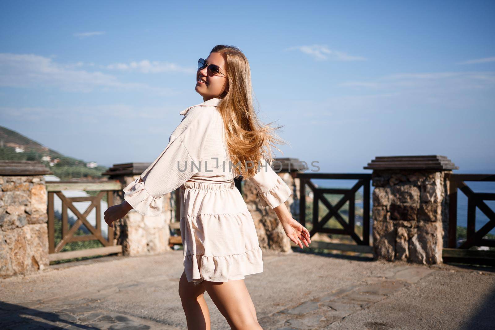 A young woman with long blond hair in a top and a skirt is walking on a summer sunny day. Happy girl with a smile on her face and in sunglasses is walking on a sunny day