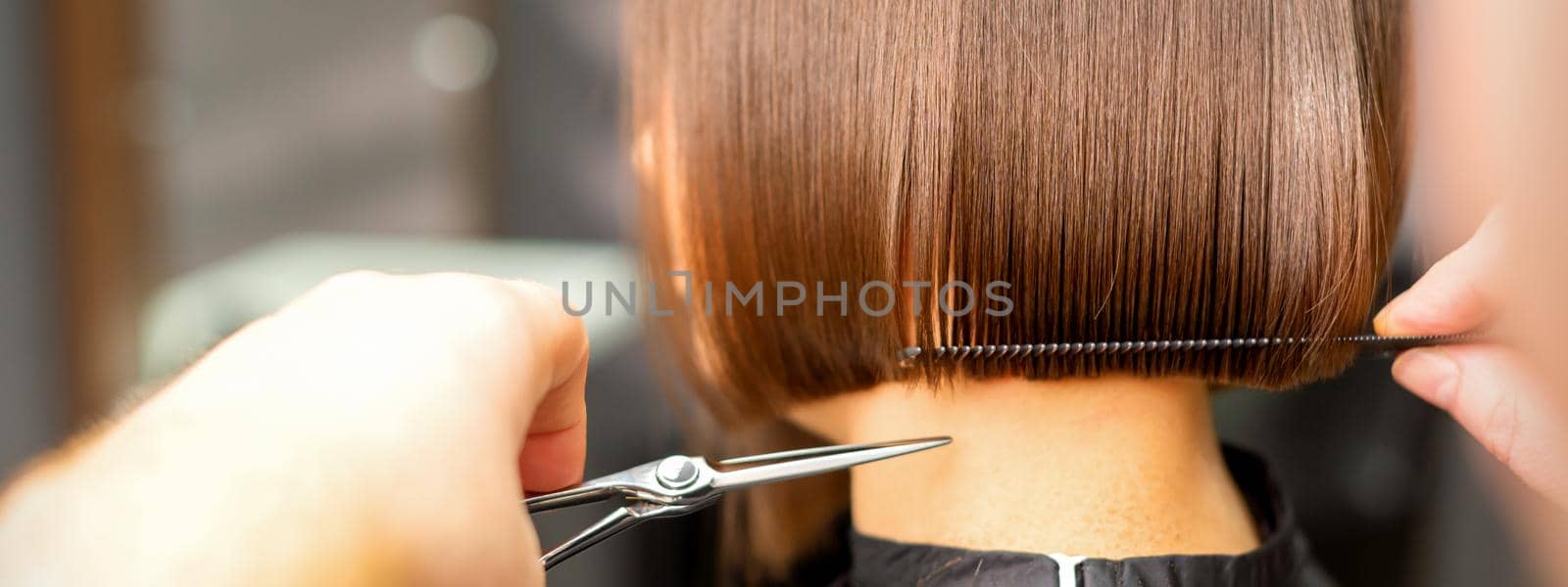 Haircut of short hair of young white woman by hands of a hairdresser in a hair salon, back view, close up