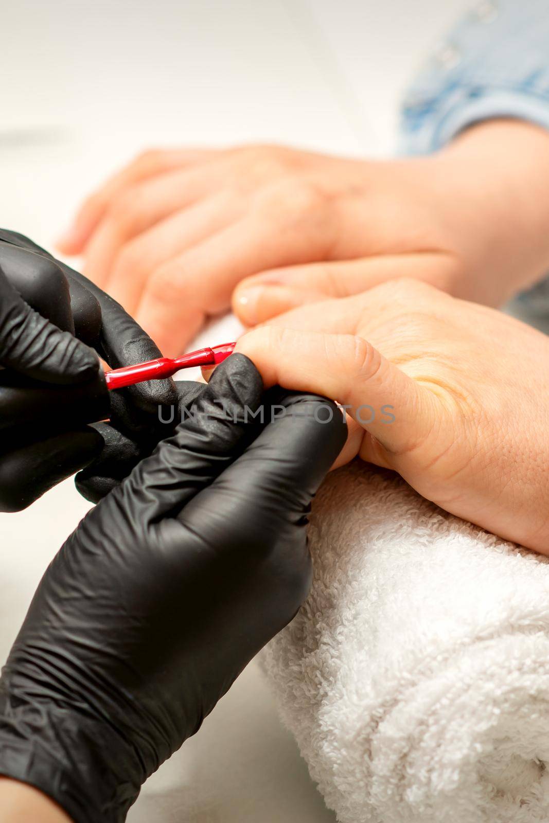 Manicure varnish painting. Close-up of a manicure master wearing rubber black gloves applying red varnish on a female fingernail in the beauty salon