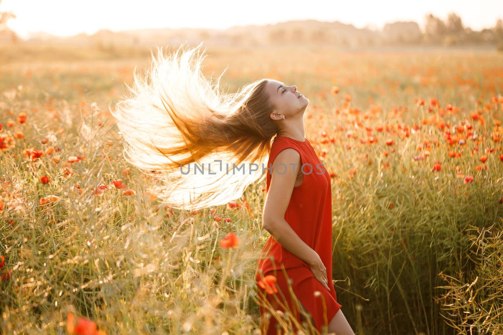 Beautiful woman in a red dress in a field of blooming poppies. Selective focus