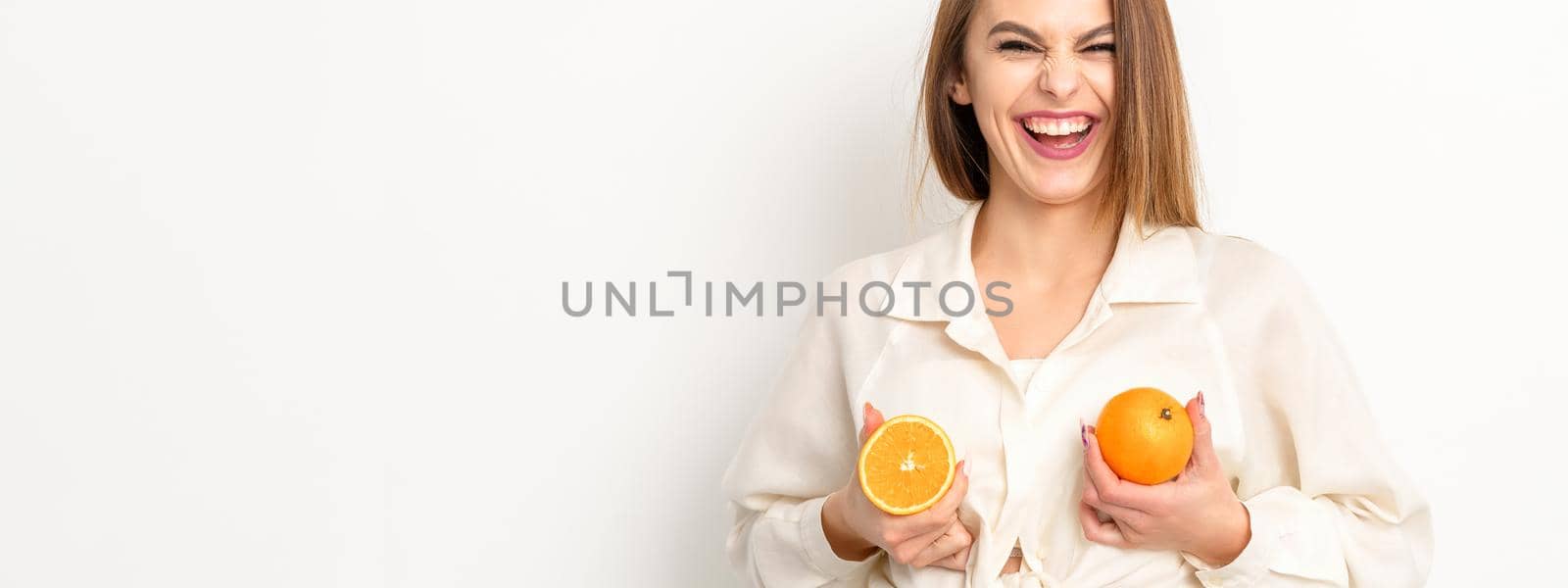 Young Caucasian smiling woman holding slices orange over isolated white background, breast health concept