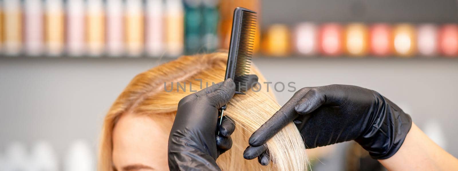 Beautiful young blonde woman with long straight blonde hair getting a haircut at the hairdresser salon. by okskukuruza