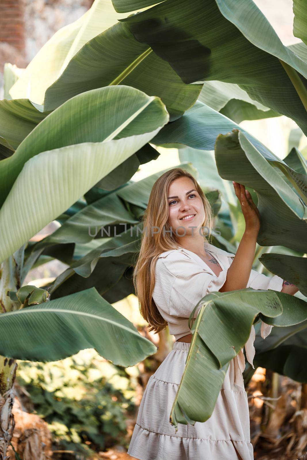 Beautiful woman in the jungle. A resort or hotel with tropical trees and plants. Woman with near banana leaf. Girl on vacation in the rainforest