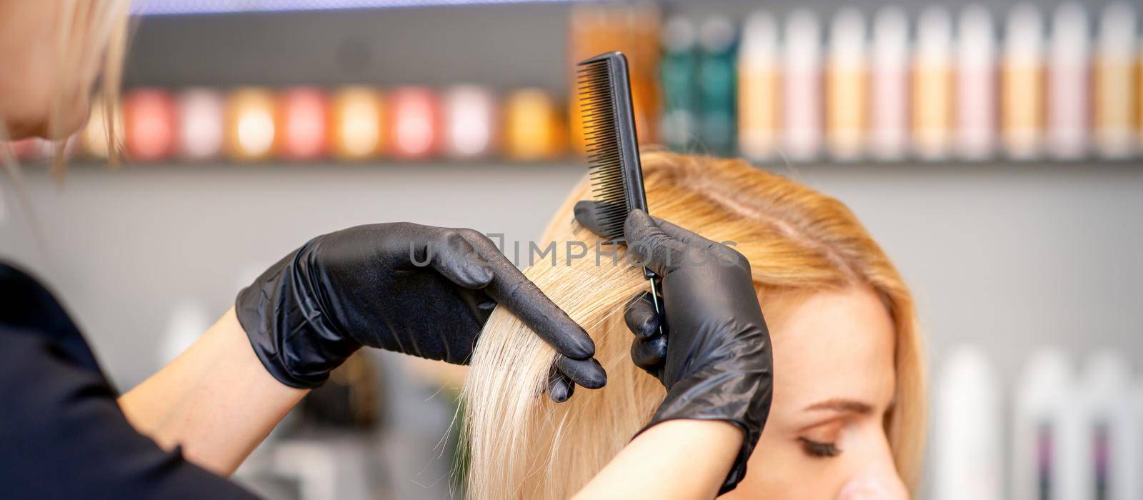 Beautiful young blonde woman with long straight blonde hair getting a haircut at the hairdresser salon. by okskukuruza