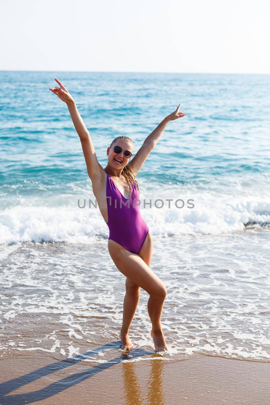 An attractive young woman comes out of the sea in a swimsuit. A girl in a swimsuit walks under the bright summer sun along the sand of the Mediterranean coast. Rest by the sea. Selective focus