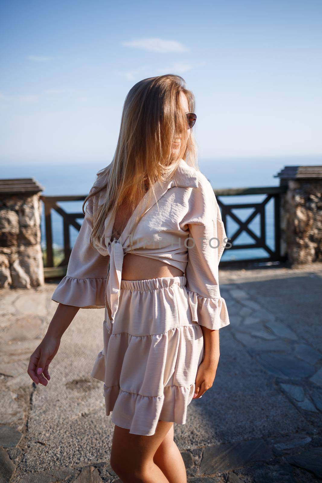 Young woman with long blond hair in a light top and skirt walks on a summer sunny day