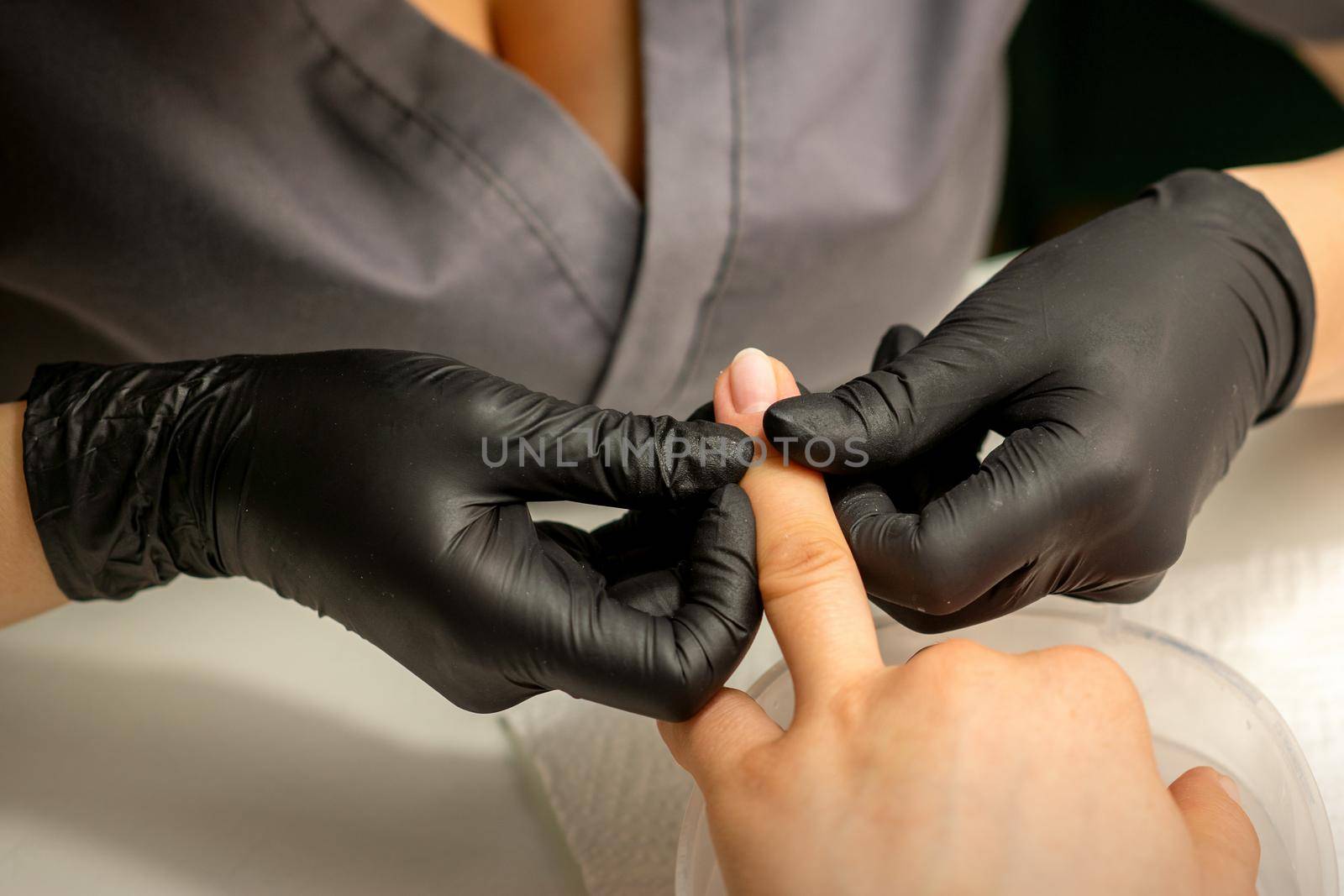 Close up professional manicure master holds the female hand of the customer and checks the manicure in a nail salon