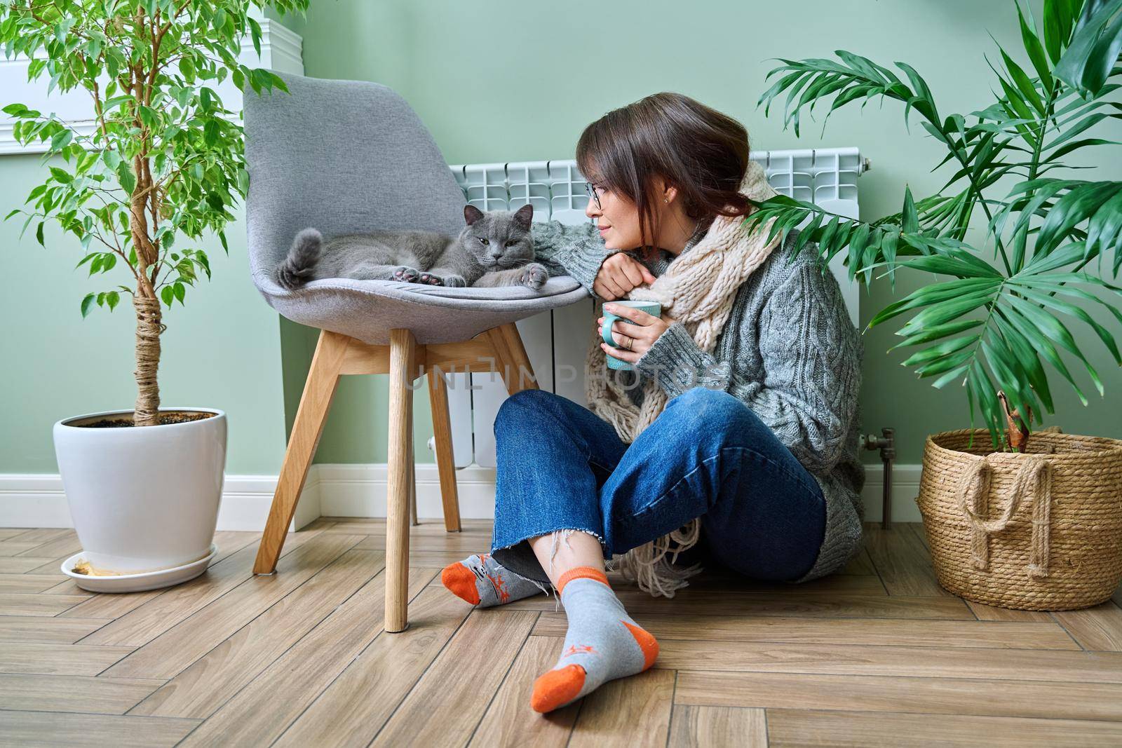 Cold winter season, woman with cat on chair near heating radiator by VH-studio