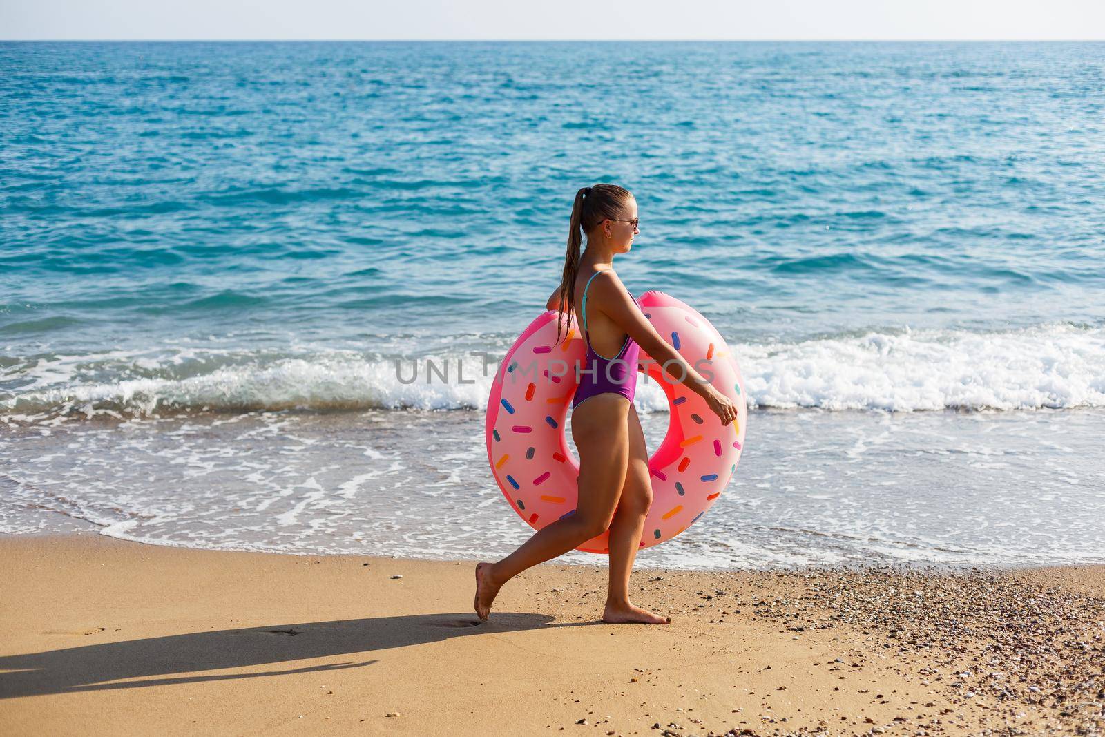 Woman on the beach walks with an inflatable ring in the sea, walks relaxing in a tropical paradise for relaxation. Young model sunbathing on summer vacation.
