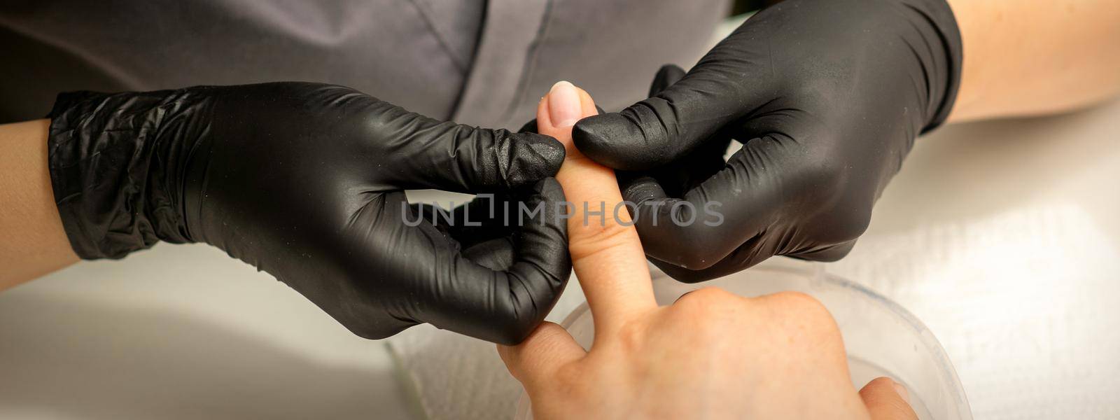 Close up professional manicure master holds the female hand of the customer and checks the manicure in a nail salon