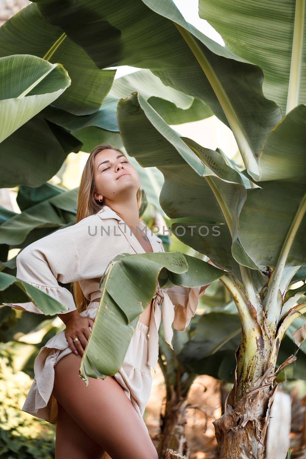 Beautiful woman in the jungle. A resort or hotel with tropical trees and plants. Woman with near banana leaf. Girl on vacation in the rainforest