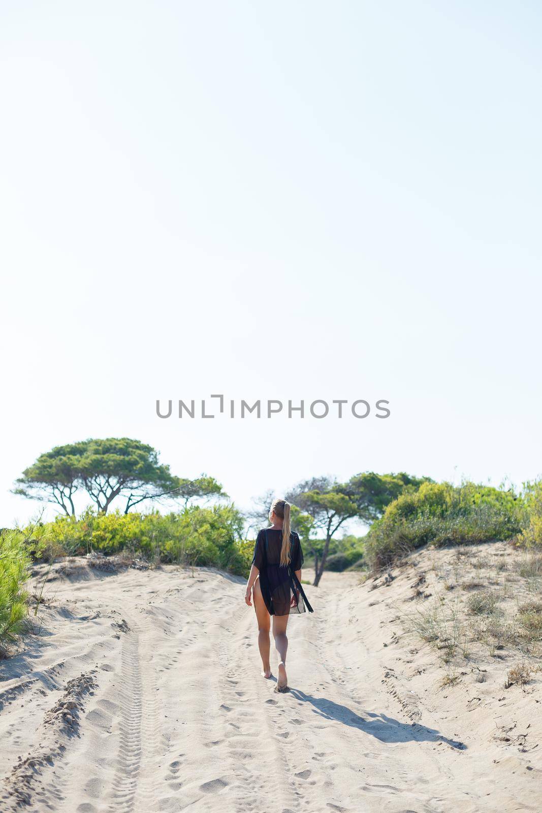 A slender tanned young woman in a swimsuit and a pareo, standing on the golden sand in the desert. Model woman resting and sunbathing on vacation. Travel concept, swimwear