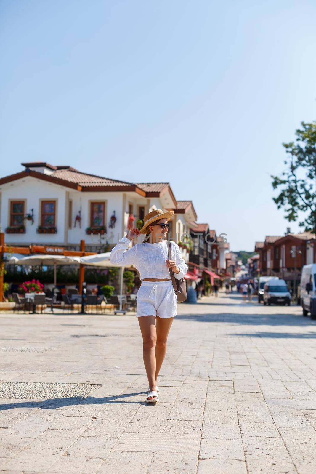 A young slender tanned woman in white shorts and a T-shirt, wearing sunglasses and a hat. Walk on a hot sunny day in the ancient city by Dmitrytph
