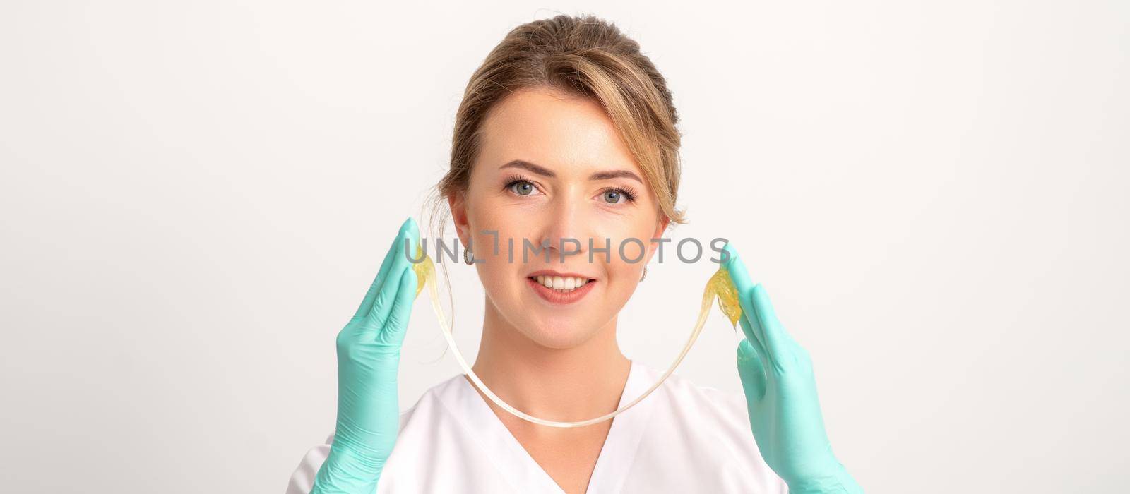 Young caucasian smiling female beautician holding wax for depilation over white background. Yellow sugar paste in hands master of depilation. Epilation concept