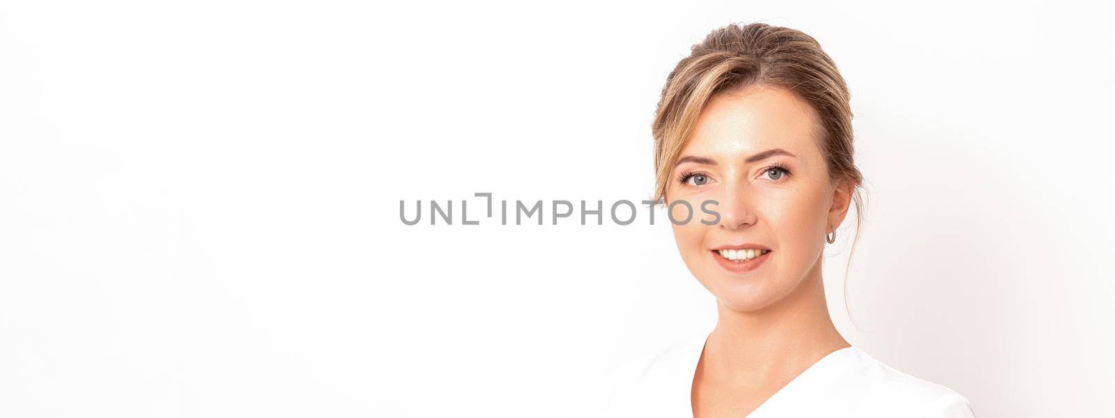 Close-up portrait of young smiling female caucasian healthcare worker standing staring at the camera on white background