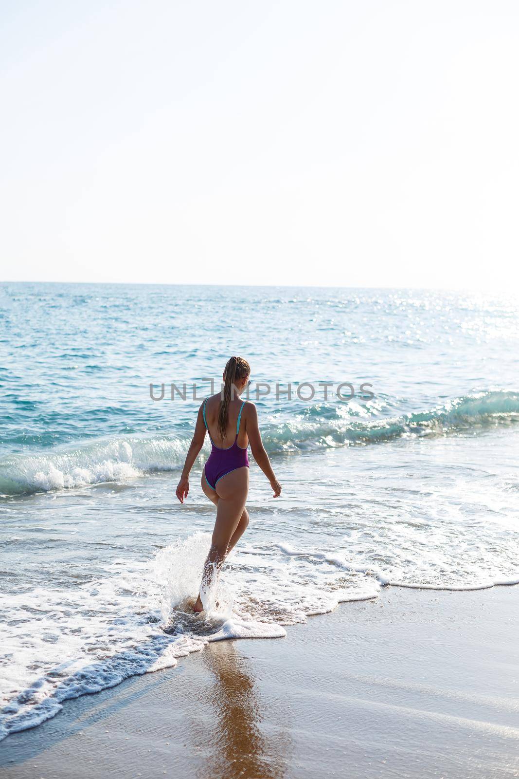 A young beautiful woman with a toned body in a bright swimsuit walks along the sandy beach. Summer vacation at the sea. Mediterranean Turkish Sea. Selective focus