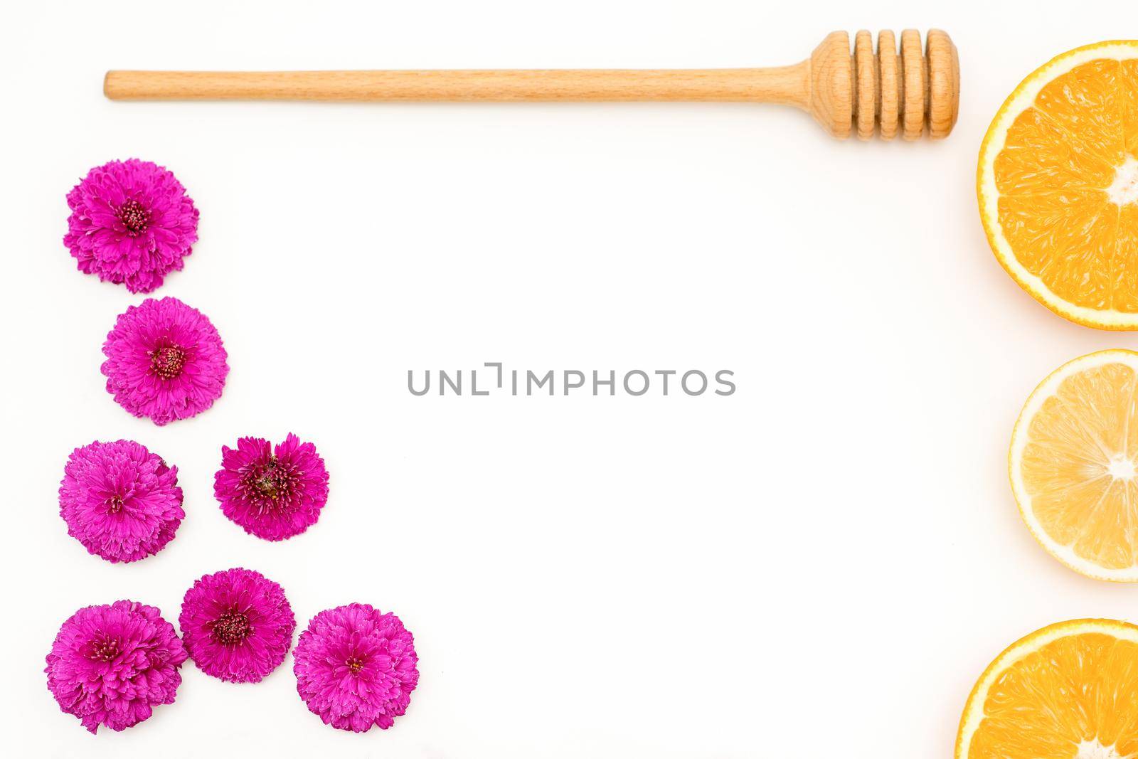 A flat lay of slices of orange fruit with red orchid petals and a wooden honey spoon lying on white background, copy space