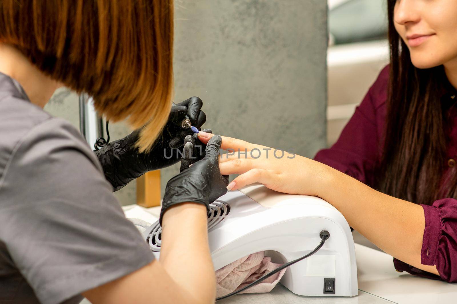Manicure master in rubber gloves applies an electric nail file to remove the nail polish in a nail salon. by okskukuruza