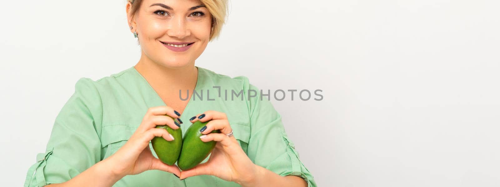 Female nutritionist doctor wearing green workwear holding green organic avocado fruit. Healthy lifestyle concept