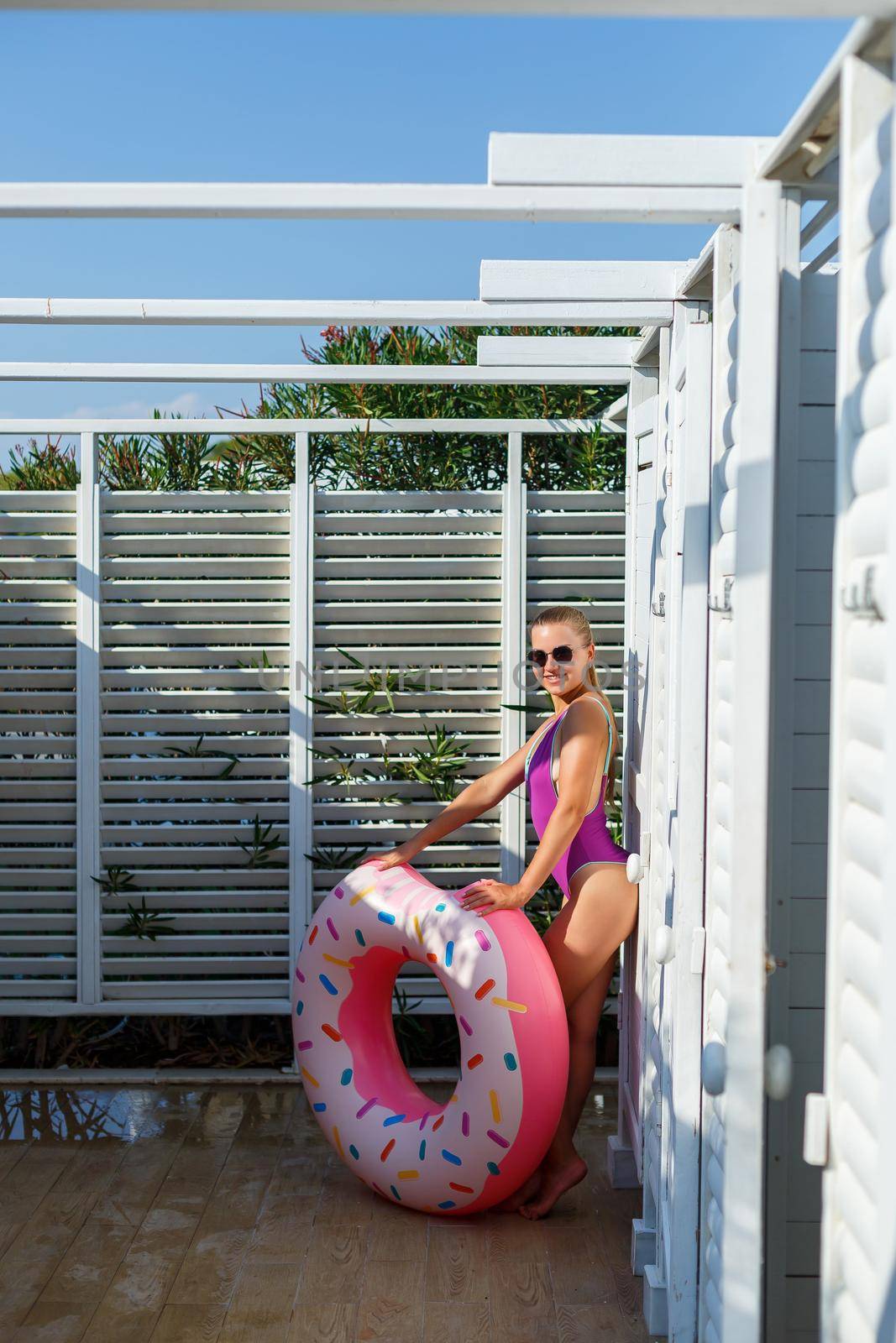 Happy young woman in stylish sunglasses and swimsuit with inflatable ring on vacation. Attractive tender girl in the sun, sunbathing and relaxing by Dmitrytph