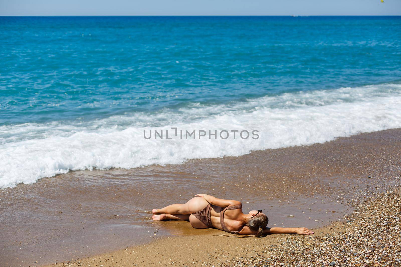 An attractive young woman in a bikini lies on the sand by the sea, relaxing on a deserted beach. Beautiful model in a swimsuit resting on the fine sand on a tropical island
