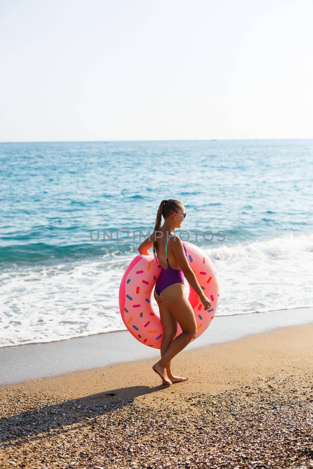 Woman on the beach walks with an inflatable ring in the sea, walks relaxing in a tropical paradise for relaxation. Young model sunbathing on summer vacation.