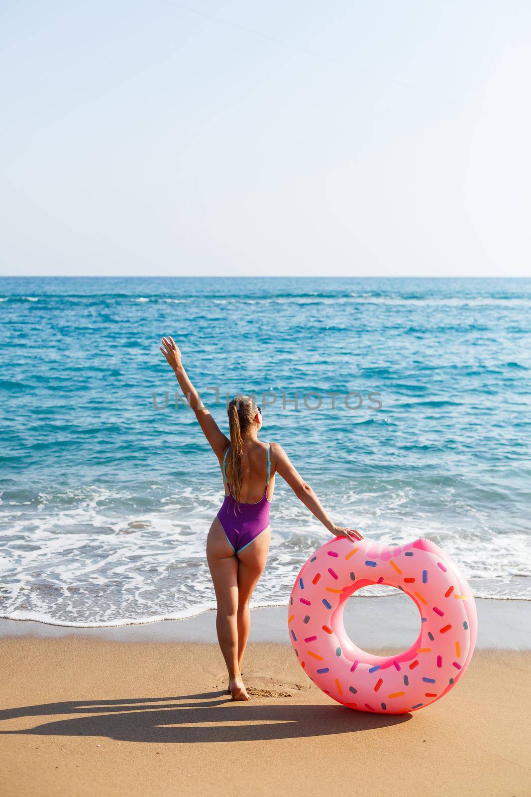 Attractive young woman in a bright swimsuit posing on the beach with an inflatable ring. Beautiful blond woman with long hair relaxing by the ocean. The concept of a sports model, swimwear