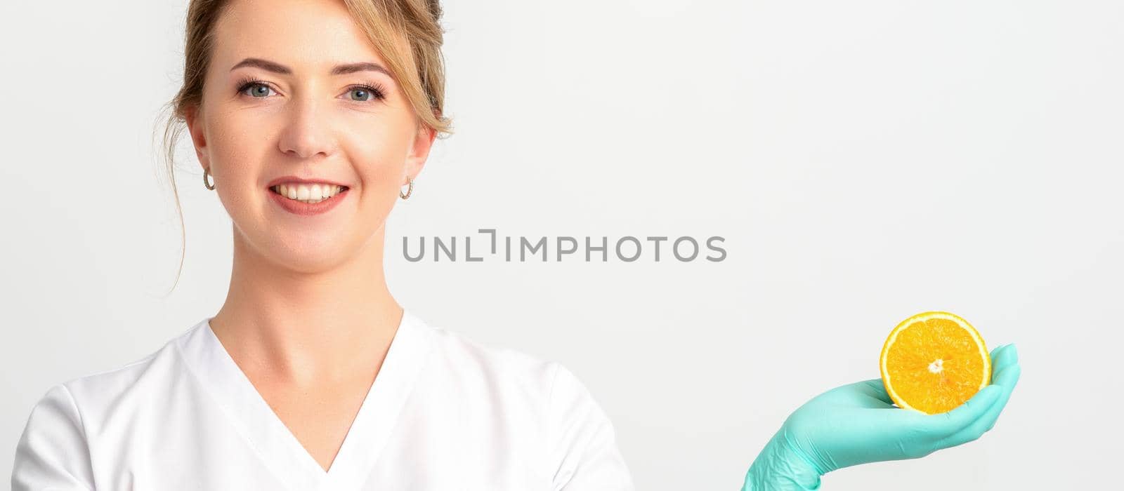 Smiling female nutritionist holding a sliced orange, looking at camera over white background, healthy diet concept