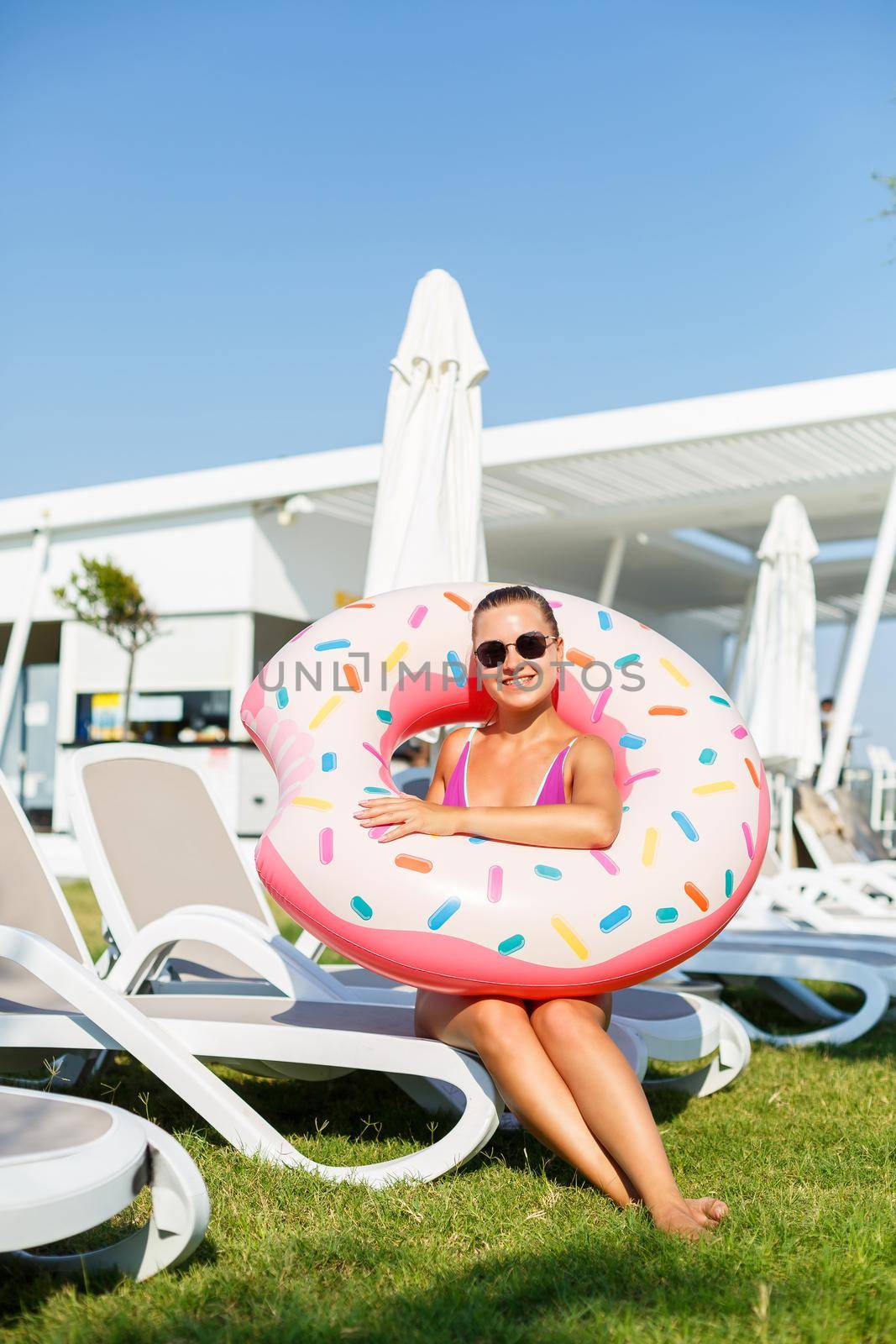A slender young woman holds an inflatable circle in her hands, standing on the green grass. Attractive model with perfect body. Vacation concept, girl goes swimming in the sea