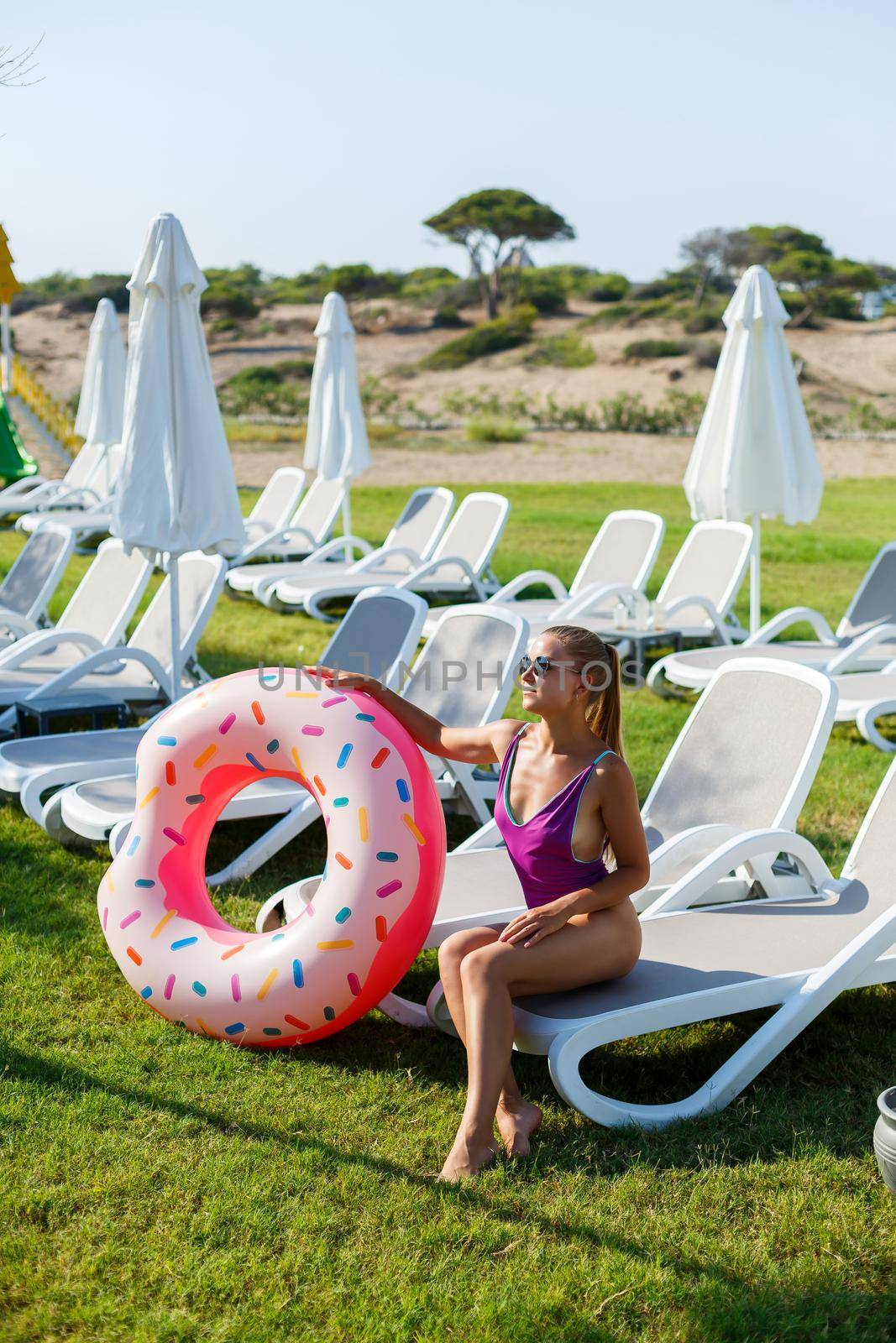 A slender young woman holds an inflatable circle in her hands, standing on the green grass. Attractive model with perfect body. Vacation concept, girl goes swimming in the sea