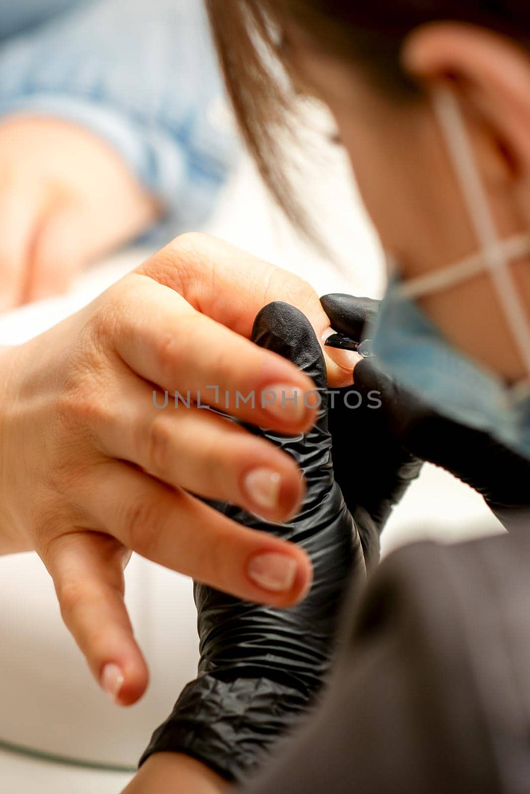 Manicure painting process. Manicure master paint the nails with transparent varnish in a nail salon, close up. by okskukuruza