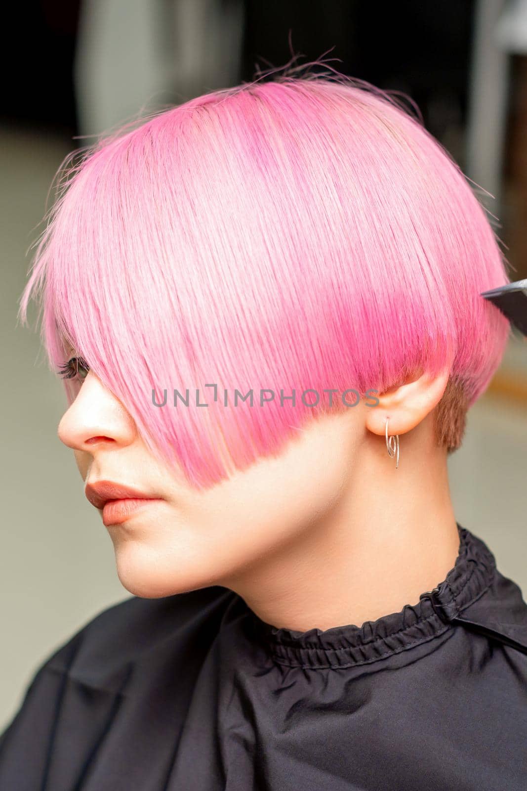 A hairdresser is combing the dyed pink short hair of the female client in a hairdresser salon. by okskukuruza